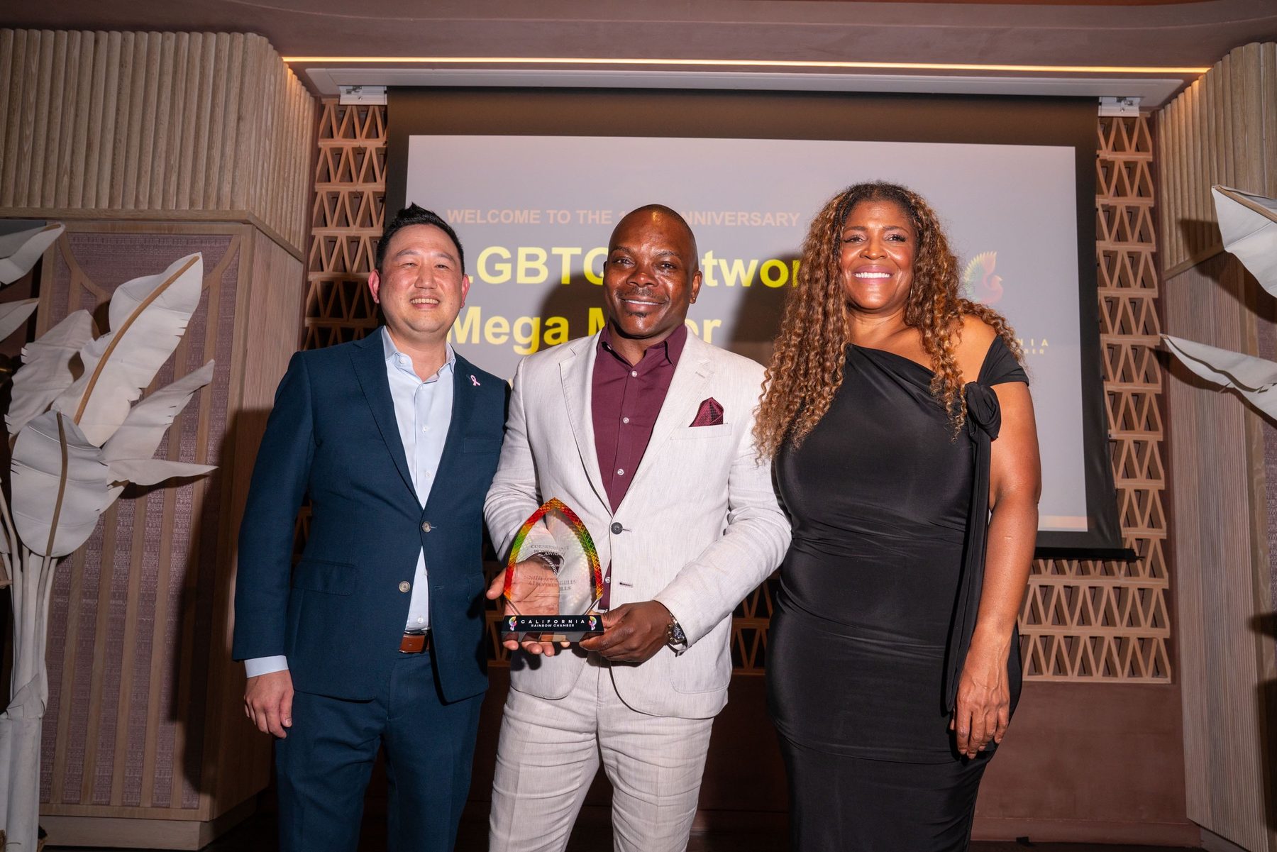 Three people on stage with a Chamber award in front of the anniversary screen